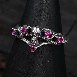May include: A silver skull ring with pink gemstones set in a twisted branch design.