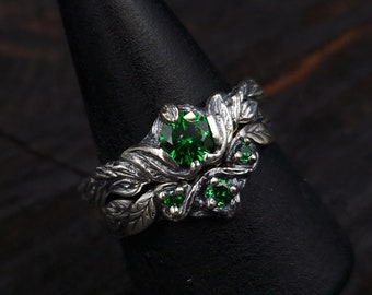 May include: A silver ring with a large green gemstone surrounded by smaller green gemstones. The ring is designed to look like a branch with leaves.