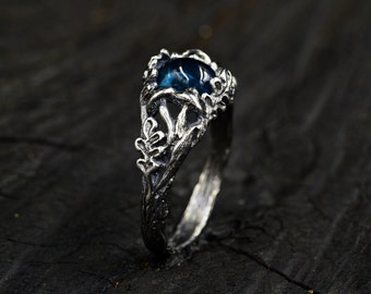 Puede incluir: Un anillo de plata con una piedra preciosa azul engastada en un diseño detallado con forma de árbol.