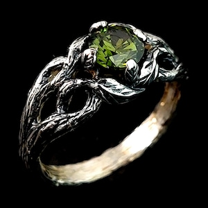 May include: A silver ring with a green gemstone set in a tree branch design.