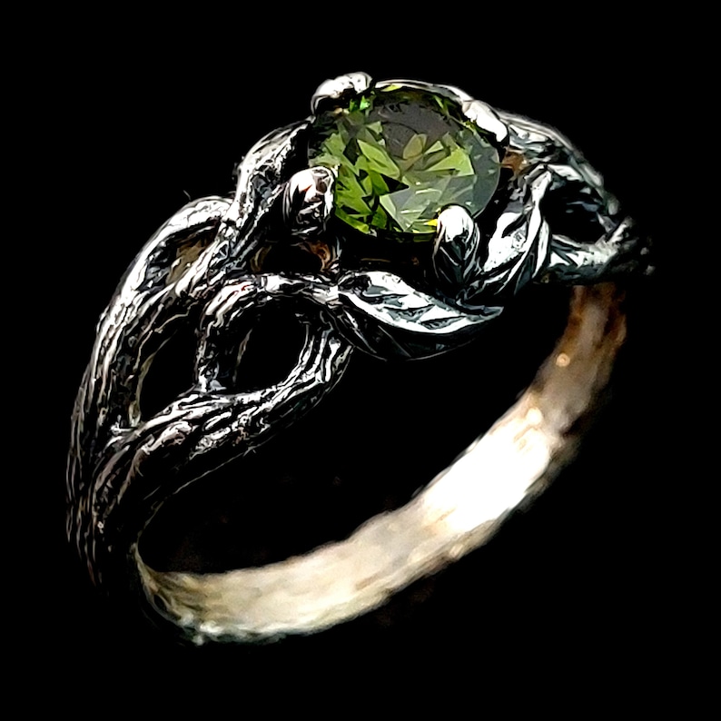 May include: A silver ring with a green gemstone set in a tree branch design.