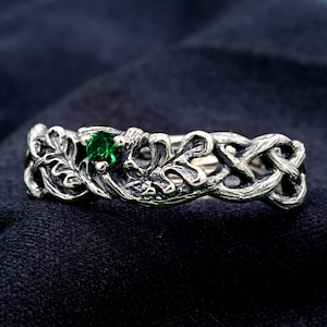 Może przedstawiać: Srebrny pierścionek z zielonym kamieniem szlachetnym osadzonym w wzorze splecionych gałęzi i liści.