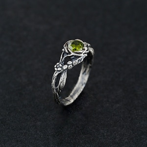May include: A silver ring with a green gemstone set in a twisted branch design.