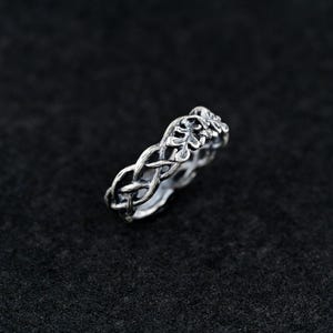 May include: A silver ring with a braided design featuring a leaf motif.