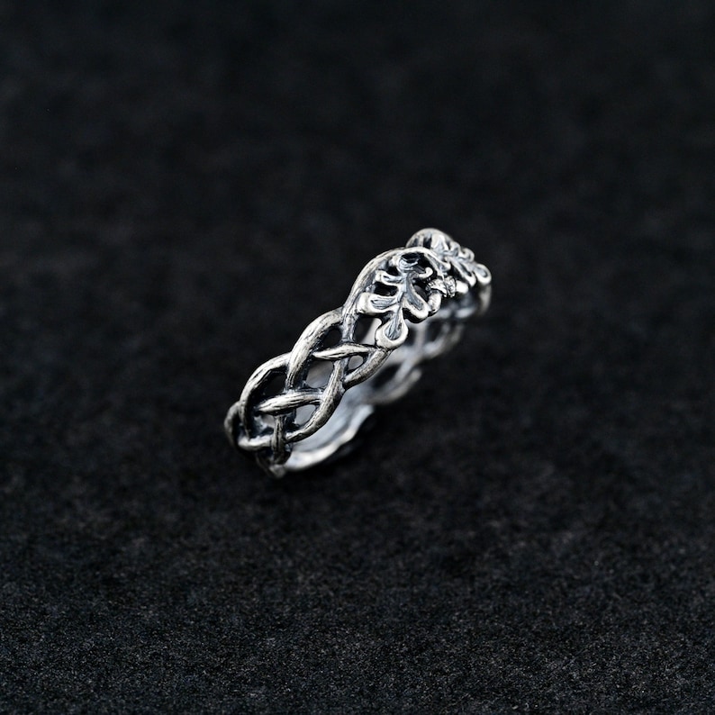 May include: A silver ring with a braided design featuring a leaf motif.
