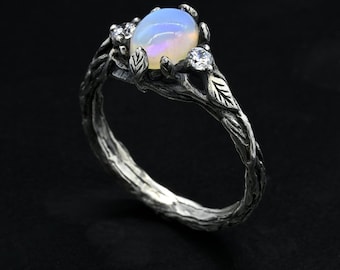 May include: A silver ring with a delicate, twig-like band and a large oval opal gemstone. The ring is accented with two smaller, round, clear gemstones.
