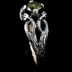 May include: A silver ring with a green gemstone set in a twisted branch design.