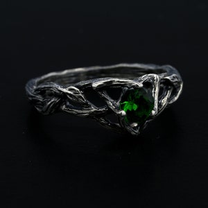 Puede incluir: Un anillo de plata con una piedra preciosa verde engastada en un diseño de rama retorcida.