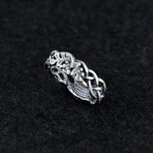 May include: A silver ring with a tree of life design. The ring is made of intricate details and features a braided band with leaves.
