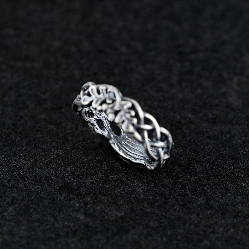 May include: A silver ring with a tree of life design. The ring is made of intricate details and features a braided band with leaves.
