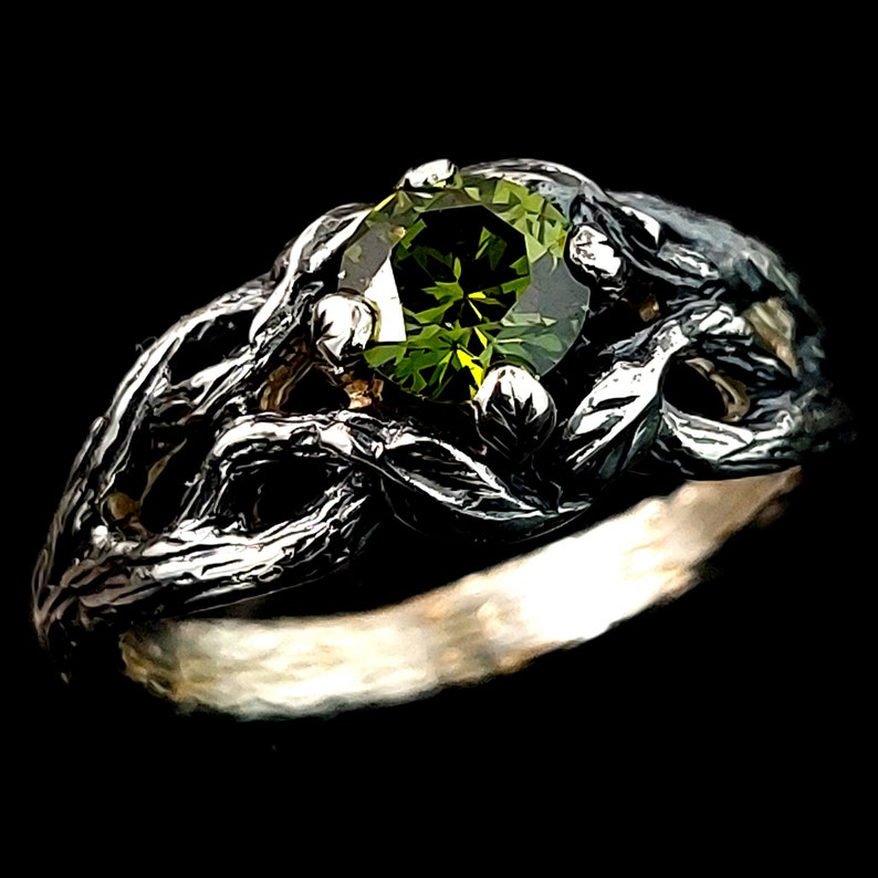 May include: A silver ring with a green gemstone set in a twisted branch design.