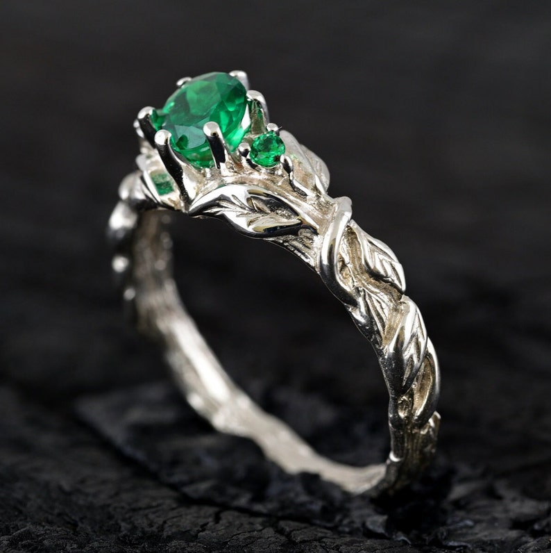 May include: A silver ring with a green gemstone and intricate leaf details. The band is twisted and resembles a vine.