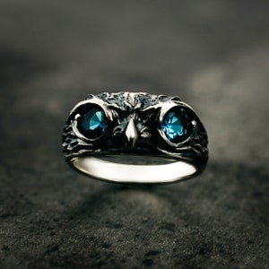May include: A silver ring featuring an owl design with two blue gemstones for eyes.