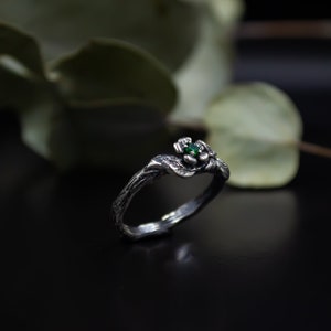 May include: A silver ring with a green gemstone set in a flower design. The ring is shaped like a twisted branch.