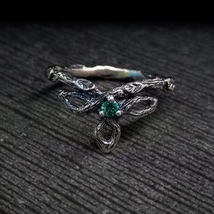 May include: A silver ring featuring a twig design with a green gemstone.