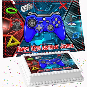 May include: A white frosted cake with a colourful gaming-themed design. The cake features a blue game controller, a red and black background, and the text "HAPPY 12TH BIRTHDAY JOSHUA". Colourful confetti is scattered around the cake.
