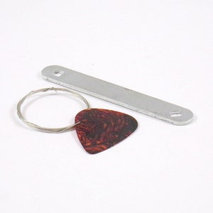May include: A silver guitar tuning wrench, a brown guitar pick, and a silver wire wound around a circle.