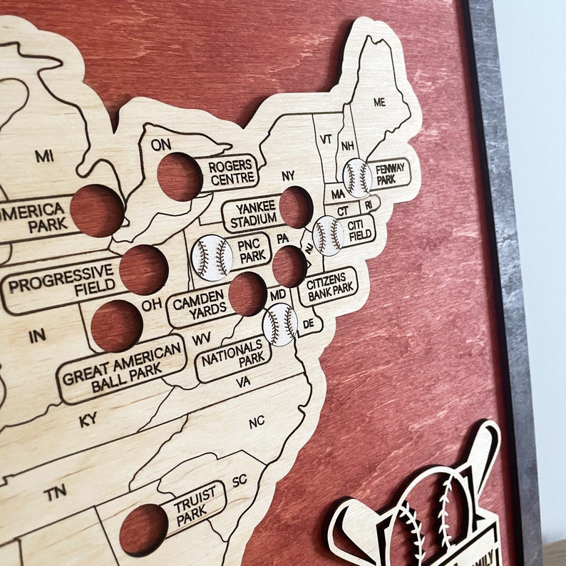 May include: A wooden map of the United States with baseball stadiums marked. Each stadium is represented by a small circle with a baseball inside. The map is stained a dark reddish brown color. The map is surrounded by a dark brown frame.