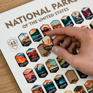 May include: A National Parks of the United States wooden map featuring a grid of hexagonal slots. Each slot contains a colorful illustrated wooden badge representing a specific park. One badge labeled Capitol Reef is being placed into its slot.