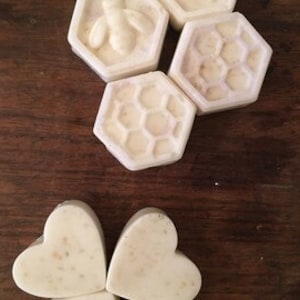 May include: Four white soap bars with a honeycomb design and a bee design. Two of the bars are shaped like hexagons and two are shaped like hearts.