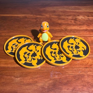 May include: Four orange and black round coasters with a silhouette of a Pokemon character. The coasters are on a wooden surface with a small orange Pokemon figurine in the center.