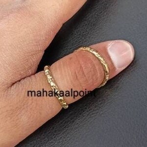 May include: Two gold thumb rings with a textured design. The rings are worn on the thumb of a hand.