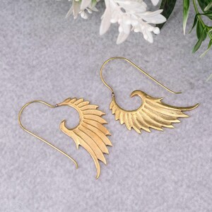 Könnte beinhalten: Ein Paar goldfarbene Ohrringe mit Flügeldesign. Die Ohrringe sind aus Metall und haben einen schlichten, eleganten Stil.