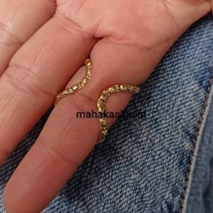 May include: Gold ring with a textured, wavy design. The ring is worn on the middle finger of a hand.