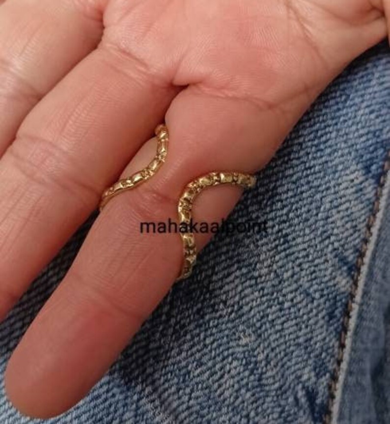 May include: Gold ring with a textured, wavy design. The ring is worn on the middle finger of a hand.
