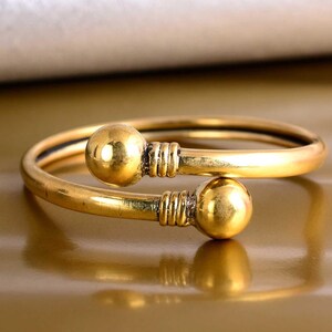 May include: A gold-toned bangle bracelet with two round, decorative accents. The bracelet is made of a thick, twisted metal.