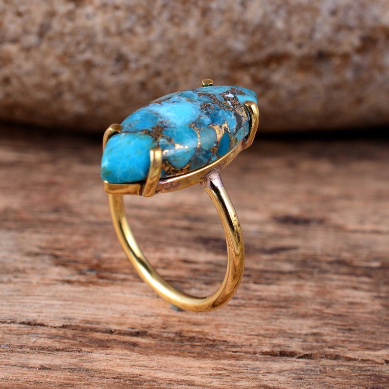 Puede incluir: Un anillo de oro con una gran piedra turquesa de forma ovalada. La piedra preciosa tiene un patr&oacute;n de m&aacute;rmol azul y marr&oacute;n.