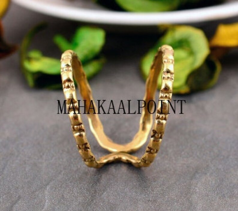 May include: A gold ring with a textured design. The ring is made of two bands that are connected at the top.