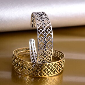 Könnte beinhalten: Zwei silberne und goldene Armbänder mit geometrischem Muster. Die Armbänder sind übereinander gestapelt.