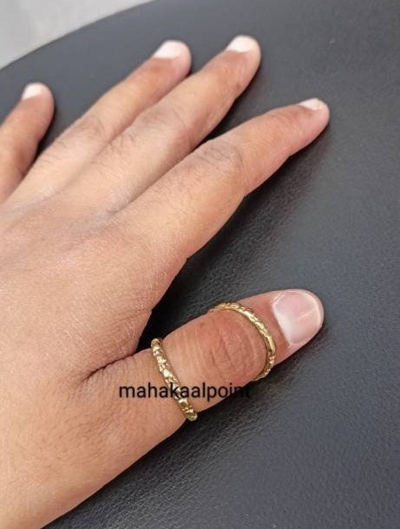 May include: Two gold thumb rings with a textured design. The rings are worn on the thumb of a hand.