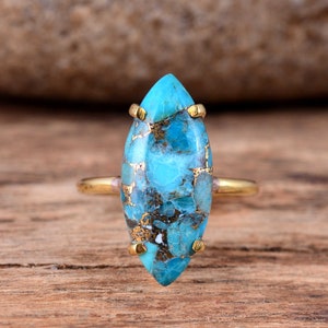 Puede incluir: Un anillo de oro con una piedra turquesa de forma marquesa. La piedra preciosa es de color azul y verde con inclusiones marrones y blancas.