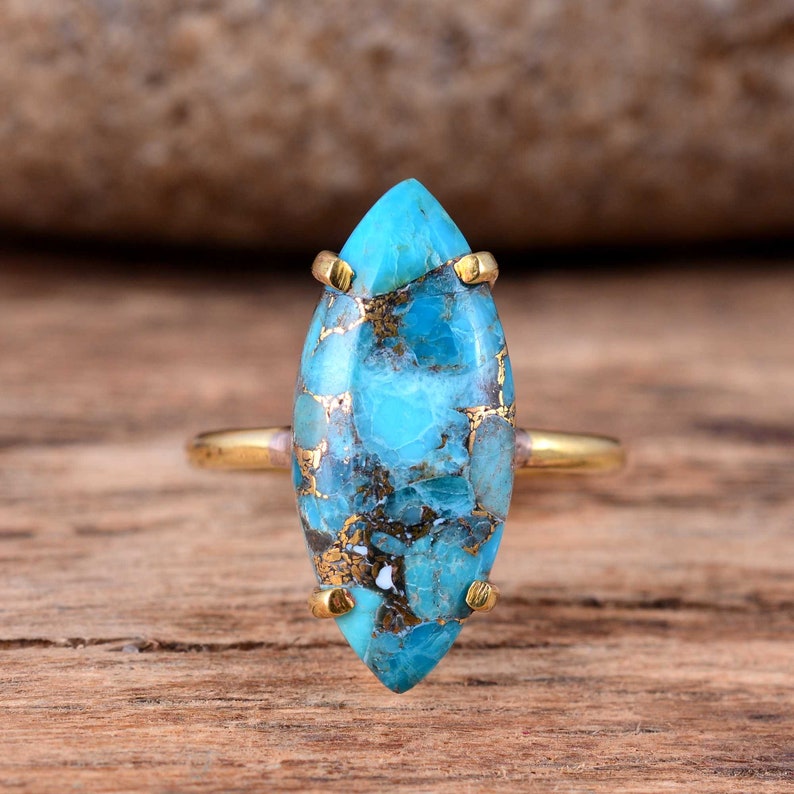 Puede incluir: Un anillo de oro con una piedra turquesa de forma marquesa. La piedra preciosa es de color azul y verde con inclusiones marrones y blancas.