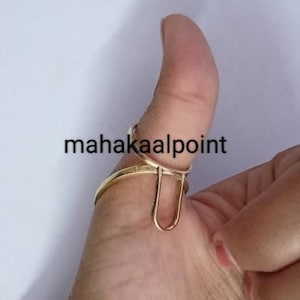 Könnte beinhalten: Goldener Daumenring mit einem einzigartigen offenen Design. Der Ring wird am Daumen einer Hand getragen.