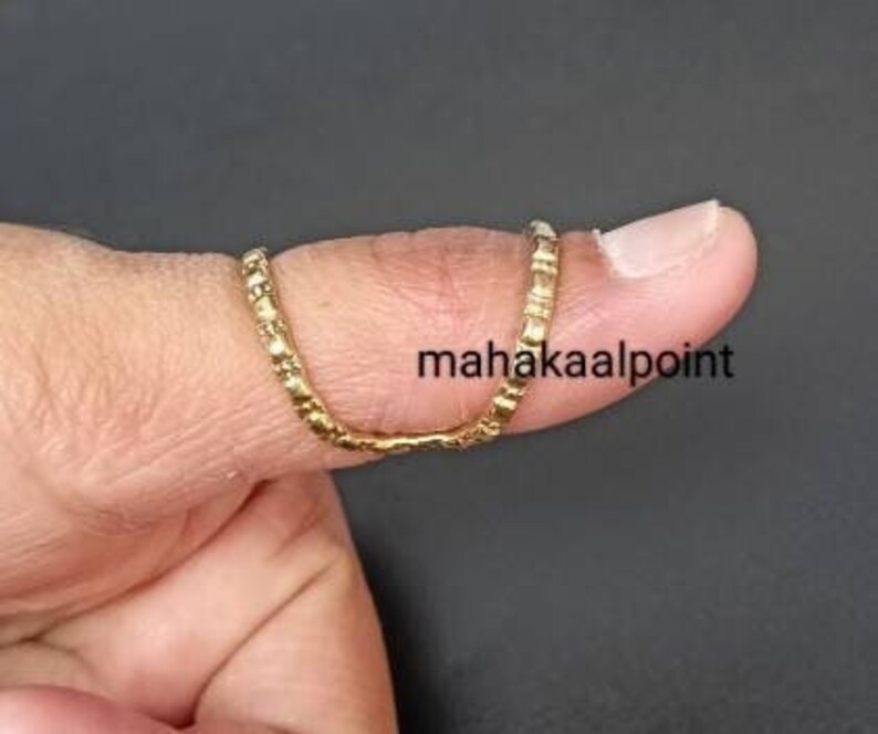 May include: A gold thumb ring with a textured design. The ring is worn on the thumb of a person's hand.