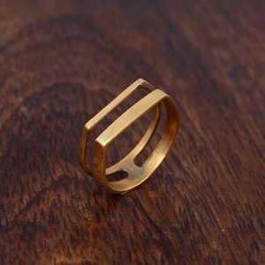 Könnte beinhalten: Ein goldfarbener Ring mit einem Doppelband-Design. Der Ring besteht aus zwei Bändern, die oben und unten miteinander verbunden sind und so eine quadratische Form bilden.