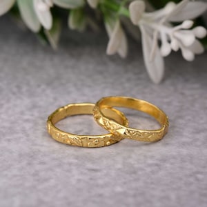 Puede incluir: Dos anillos de color dorado con un diseño floral. Los anillos están apilados uno encima del otro.