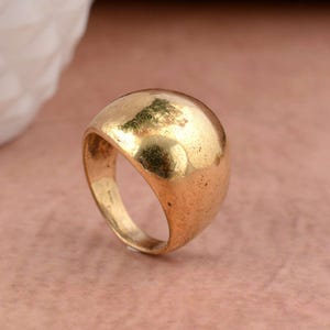 Könnte beinhalten: Ein goldfarbener Ring mit einer glatten, abgerundeten Kuppel.
