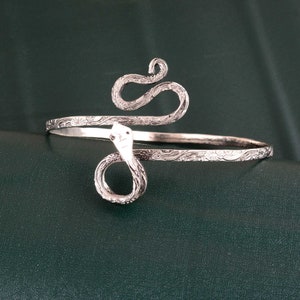 May include: Silver snake bracelet with a floral design. The snake is coiled around the wrist and has a detailed head.