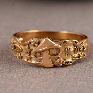 Könnte beinhalten: Ein goldfarbener Ring mit einem Pilzdesign und filigranen Details. Der Ring zeigt einen Pilz mit Stiel und Hut, umgeben von Sternen und floralen Motiven.
