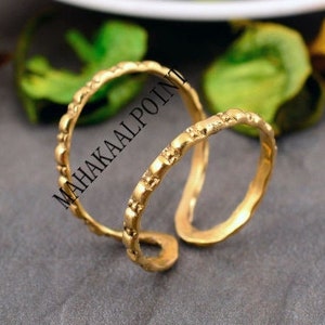 May include: Two gold-toned metal rings with a textured surface. The rings are interlocked and have a simple, minimalist design.