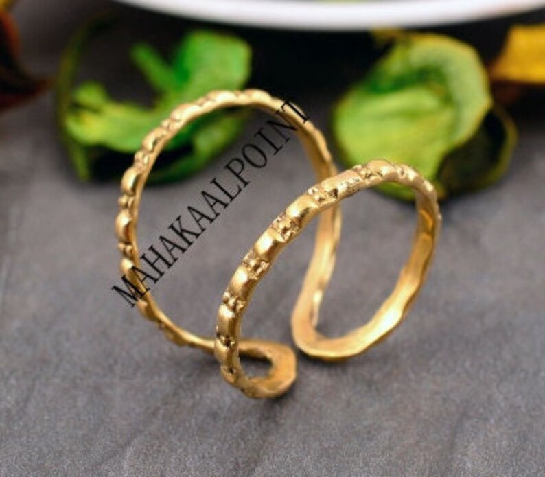 May include: Two gold-toned metal rings with a textured surface. The rings are interlocked and have a simple, minimalist design.