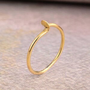 Könnte beinhalten: Ein schlichter Goldring mit einem einzigartigen, geschwungenen Design. Der Ring ist dünn und zart und wäre ein tolles Schmuckstück für jeden Tag.