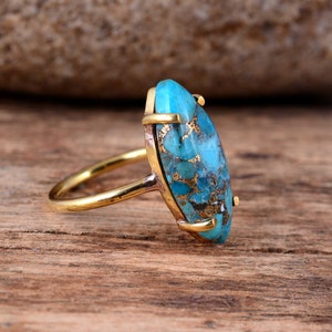 Puede incluir: Un anillo de oro con una gran piedra ovalada de turquesa. La turquesa es de color azul y verde moteado con motas doradas.