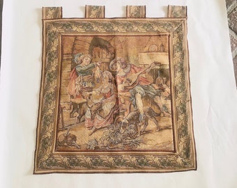 May include: A tapestry wall hanging with a beige background and a green border. The tapestry depicts a scene of people playing music and dancing in a rustic setting.