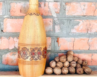 Könnte beinhalten: Eine Holzflasche mit floralem Muster und ein Haufen Walnüsse auf einem Holzregal vor einer Backsteinwand.