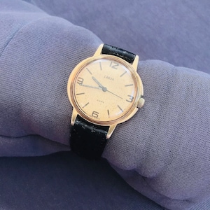May include: A gold-toned wristwatch with a black leather band. The watch face is white with black markings and the word "Carja" printed on it.